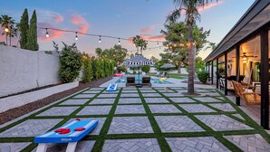 A pool area with a shuffleboard table, lounge chairs, and string lights. - Spacious Modern Oasis with Pool, Hot Tub, and Putting in Scottsdale (Phoenix)