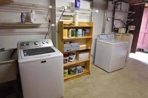 A laundry room with a Maytag washer, a dryer, and shelves with cleaning supplies.