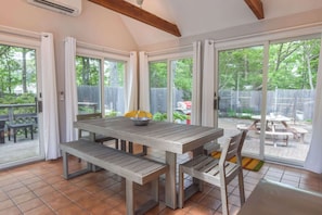 A patio area with a wooden table and benches, large sliding glass doors leading to a backyard with a barbecue grill and a wooden deck. - Sunroom Expansive Patio Fenced Yard! (Eastham)
