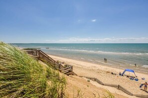 A beach with a wooden walkway leading to the shore, a sandy beach, and a clear blue sky.