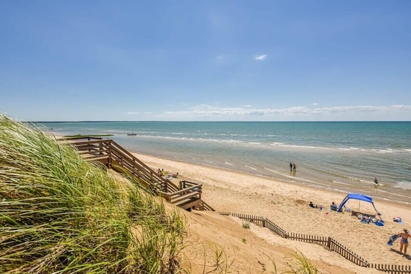 A beach with a wooden walkway leading to the shore, a sandy beach, and a clear blue sky. - Sunroom Expansive Patio Fenced Yard! (Eastham)