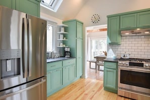 A modern kitchen with green cabinets, stainless steel appliances, and a tiled backsplash. - Sunroom Expansive Patio Fenced Yard! (Eastham)