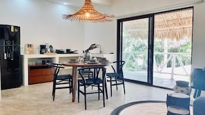 Una cocina moderna con una mesa de comedor, sillas, una lámpara colgante y un gran ventanal corredero que da a un espacio exterior.