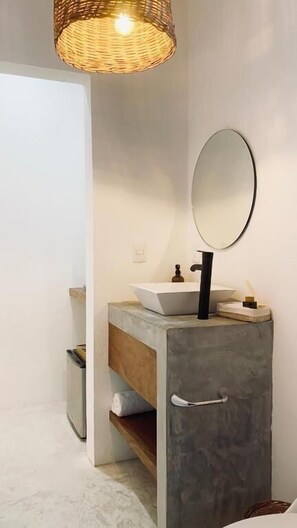 Un baño de diseño moderno, con un espejo grande, un lavamanos blanco y una lámpara de mimbre.