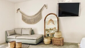 A living room with a light grey sofa, a hanging macrame wall decor, a large mirror with a wooden frame, and wicker baskets on the floor. - Casa Macay (Tulum)