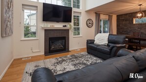 Ein Wohnzimmer mit Kamin, Flachbildfernseher, Ledersofas und einem Essbereich mit einer Kronleuchter.