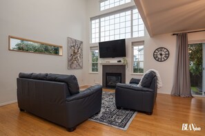 Una sala de estar moderna con chimenea, un televisor grande y un reloj en la pared.