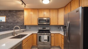 Eine moderne Küche mit Holzausbau, einem Edelstahlkühlschrank, einem Backofen, einer Mikrowelle und einem Spülbecken.