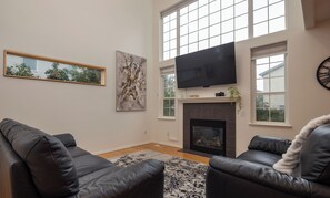 Ein Wohnzimmer mit Kamin, zwei Ledersofas, einem großen Fernseher und Bildern an den Wänden.