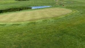 Un parcours de golf avec un étang, des arbres et un ciel dégagé.