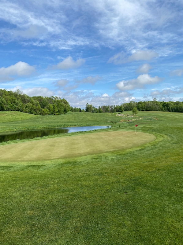 Golfkenttä, jossa on lampi, puita ja kirkas taivas.