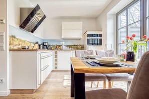 A modern kitchen with white cabinetry, a wooden countertop, and a dining area with a wooden table and chairs. - Rosenberg 13 Whg. 1d "Abendsonne am Rosenberg" - Holiday apartment "Abendsonne am (Zingst)