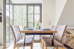 Uma sala de jantar com mesa de madeira, cadeiras estofadas e vista para árvores através de amplas janelas.