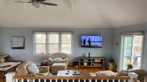 A living room with a TV, a ceiling fan, a window, and a chair.