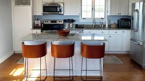 A modern kitchen with white cabinets, stainless steel appliances, a granite countertop, and three bar stools.