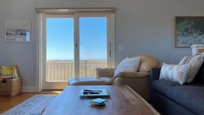 A living room with a wooden coffee table, a sofa, and a view of the sea through a sliding door.