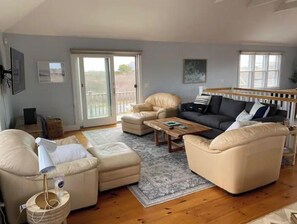 A spacious living room with a large window, a sofa set, a coffee table, and a wooden floor.
