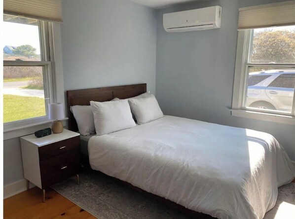 A bedroom with a bed, a nightstand, a lamp, and an air conditioning unit. - Authentic Nantucket Experience at Sunny Daze! (Nantucket)