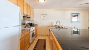 A kitchen with wooden cabinets, a white refrigerator, a stove, and a sink. - Ocean View 2 Bedroom Kahalu'u Reef KR301 (Kailua Kona)