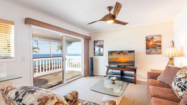 A living room with a glass coffee table, a sofa, a television, and a ceiling fan. - Ocean View 2 Bedroom Kahalu'u Reef KR301 (Kailua Kona)