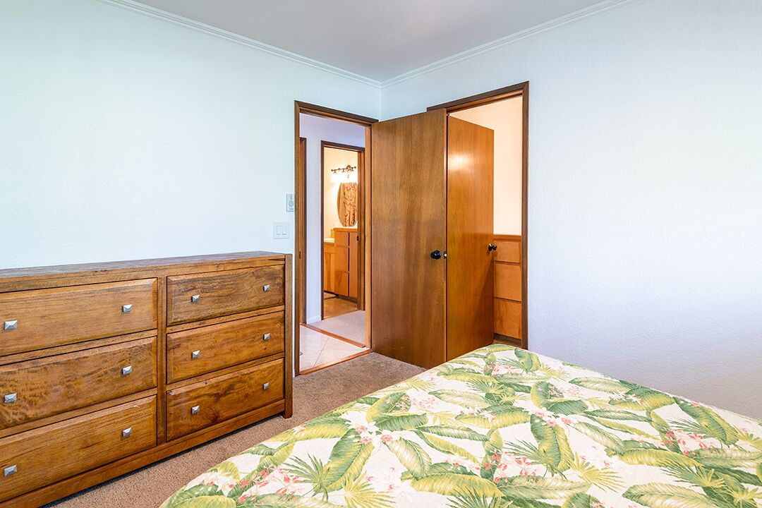 A bedroom with a wooden dresser, a bed with a floral bedspread, and a closet with a door open to a bathroom.