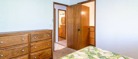 A bedroom with a wooden dresser, a bed with a floral bedspread, and a closet with a door open to a bathroom.