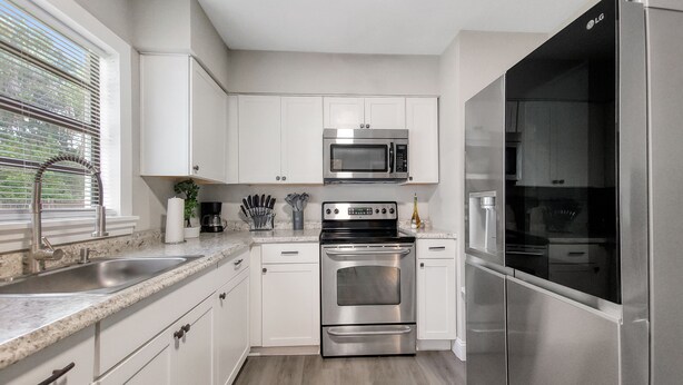 A modern kitchen with white cabinets, stainless steel appliances, a granite countertop, and a window with blinds.
