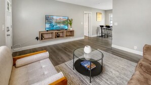 A modern living room with a grey sofa, a glass coffee table, and a flat-screen TV on a wooden shelf.