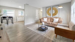 A modern living room with a beige sofa, a glass coffee table, and a dining area with a white table and black chairs.
