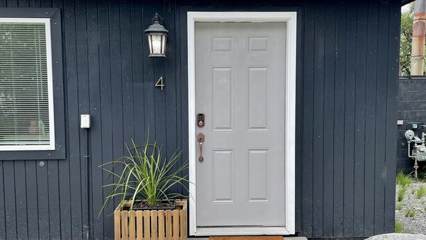 A modern house with a dark exterior, a white door, and a small porch with a bench. - Lovely apartment in the heart of Kenai (Kenai)