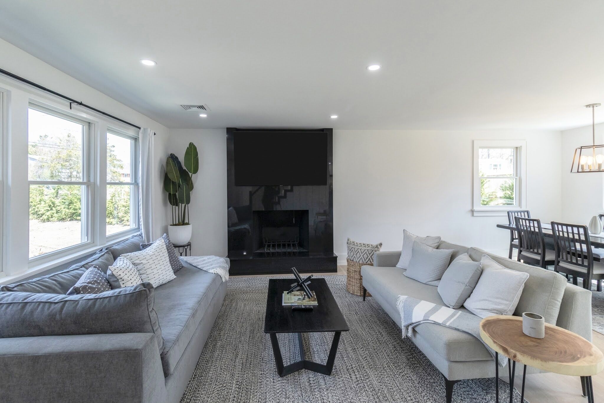Un salon moderne avec une cheminée, des canapés gris et un coin repas avec des chaises noires.