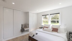 Ein Schlafzimmer mit einem großen Bett, einem Einbauschrank, einem Fenster mit Blick ins Grüne und einem Nachttisch mit Lampe.