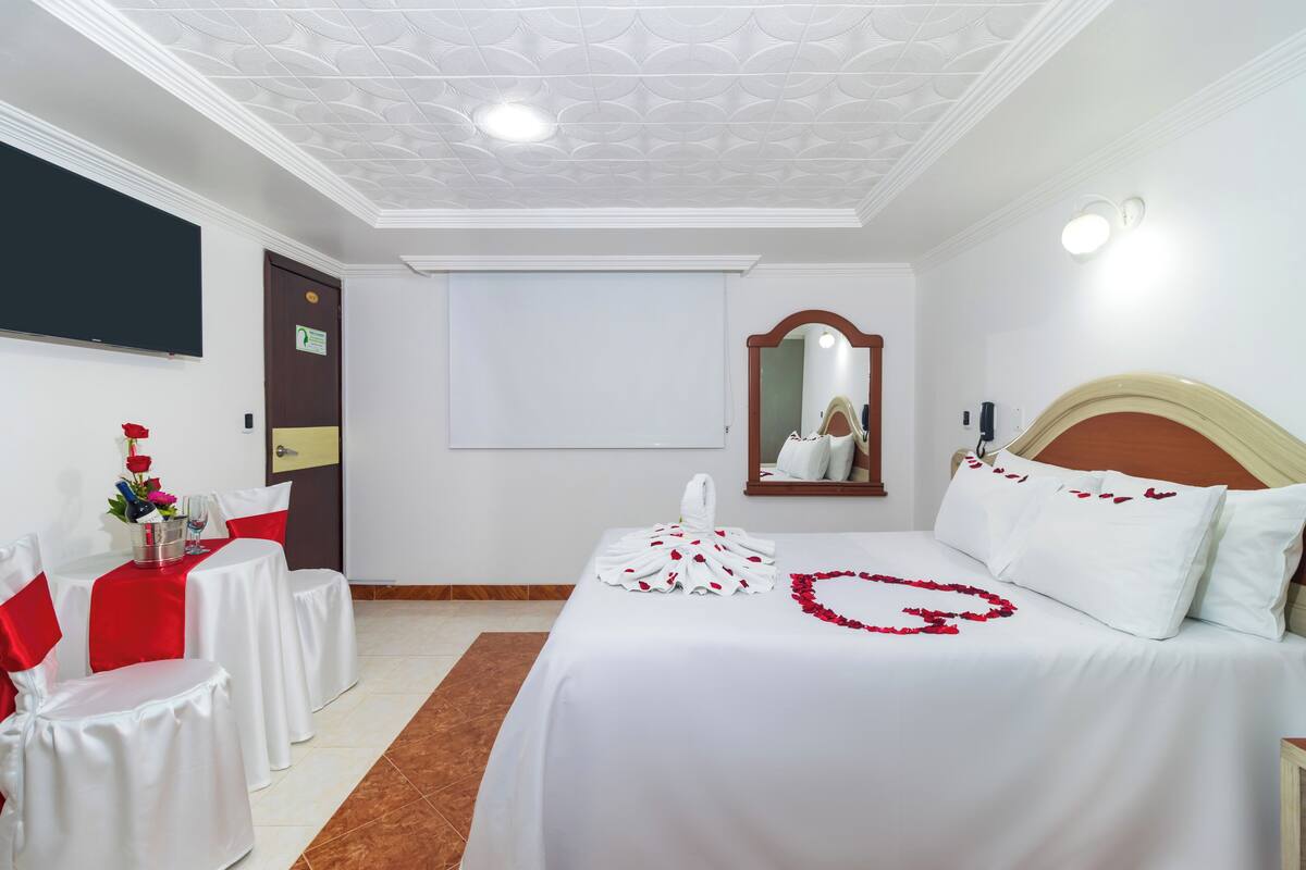 Ein Hotelzimmer mit einem ordentlich bezogenen Bett, einem kleinen Tisch mit einem roten Stuhl, einem Spiegel und einer Tür mit einem Schild.