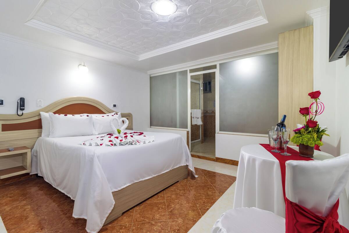 Ein Hotelzimmer mit einem Bett, einem kleinen Tisch mit Blumenvase, einem Stuhl und einem durch eine offene Tür einsehbaren Badezimmer.
