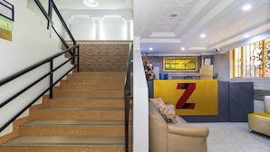 Un vestíbulo de hotel con una escalera, un mostrador de recepción y un cartel grande con la letra 'Z'.