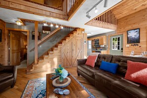 A wooden interior with a staircase, a brown leather sofa, and a dining area. - Beautiful Mountain VIEWS! Cozy! Privacy! Hot Tub! Pets OK! Pool & Fishing Pond! (Sevierville)