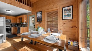 A wooden cabin interior with a dining table set for four, kitchen appliances, and a framed picture on the wall.