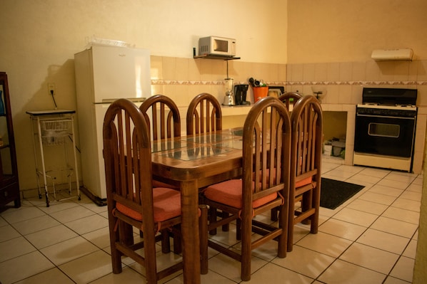 Una cocina con una mesa de comedor, sillas, un refrigerador, un microondas y un horno.