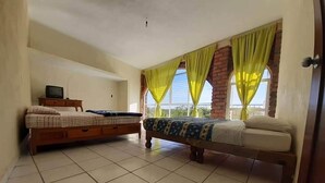 Un dormitorio con dos camas, un televisor sobre una cómoda y un balcón con cortinas amarillas.