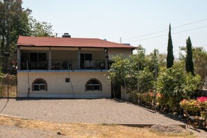 Un edificio de dos pisos con techo rojo, un balcón en el nivel superior y un patio empedrado.