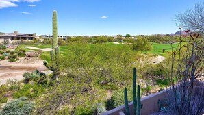 Un paysage désertique avec des cactus, un terrain de golf et, au loin, un bâtiment moderne.