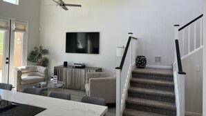 Un salon moderne comprenant un coin repas, un escalier et un téléviseur fixé au mur.