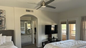 Une chambre d’hôtel avec deux lits, une télévision, un ventilateur de plafond et une salle de bain visible à travers une arche.