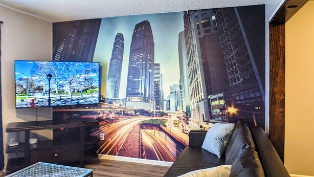 Un salon avec une grande fresque représentant un paysage urbain, un téléviseur à écran plat, un canapé en cuir noir et une table basse.