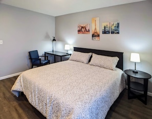 Une chambre d’hôtel avec un grand lit, deux tables de chevet avec des lampes, un bureau avec une chaise et trois œuvres d’art mural représentant des monuments célèbres.