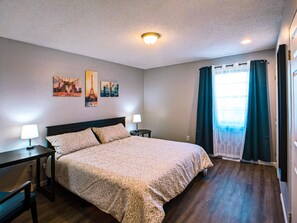 A hotel room with a large bed, two bedside tables with lamps, a ceiling light, and a window with curtains. - Cozy, clean & spacious townhouse - Unit 1 (Overland Park)