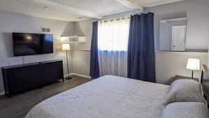 Une chambre d’hôtel avec un grand lit, un téléviseur à écran plat, une commode et une fenêtre avec des rideaux.