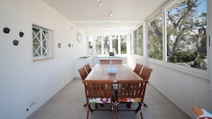 A spacious dining area with a wooden table and chairs, large windows offering views of trees, and a kitchen in the background. - WePuglia - Dimora Capitolo (Monopoli)