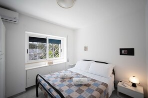 Une chambre à coucher propre et moderne, avec un lit, une table de chevet dotée d’une lampe, une fenêtre avec des stores et un panneau de commande fixé au mur.