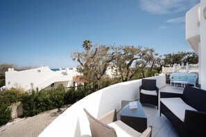 A rooftop terrace with outdoor seating, a view of the sea, and white buildings in the background.